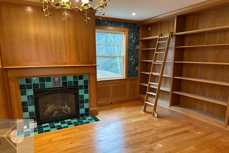 Library with custom tiled fireplace and custom library shelving and ladder.